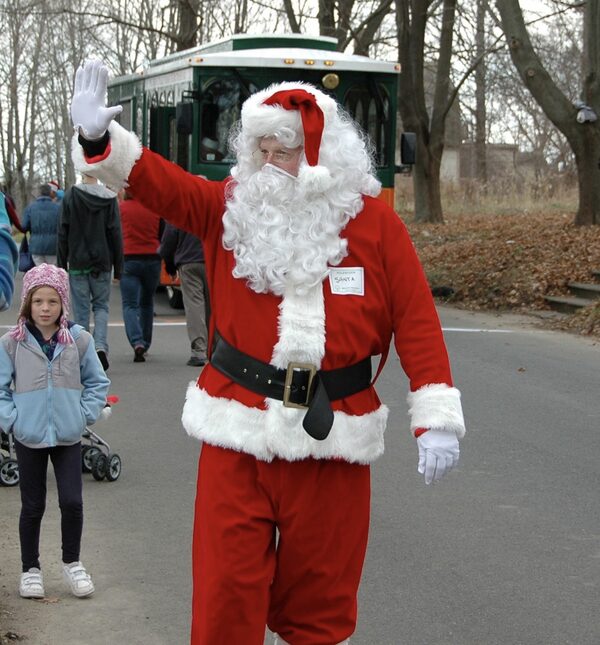 Santa Chris waving as he walks past a trolley at an outdoor community event